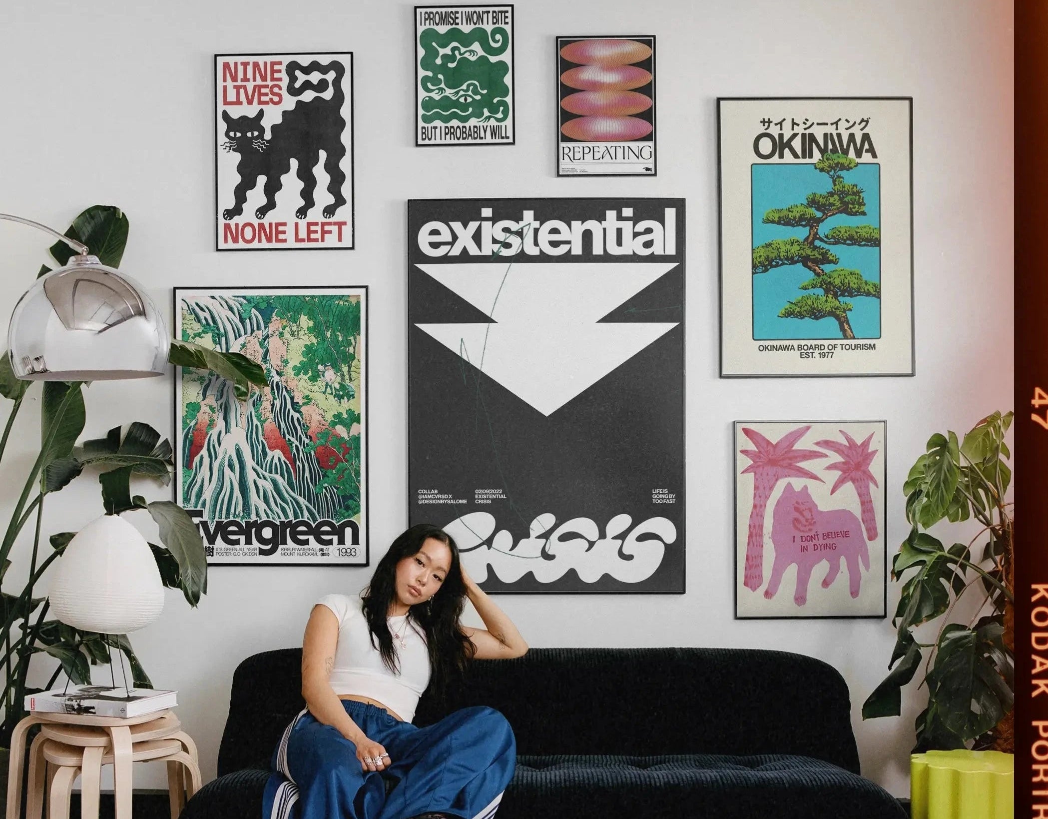 Person sitting on a black couch in a room with various posters on the wall.